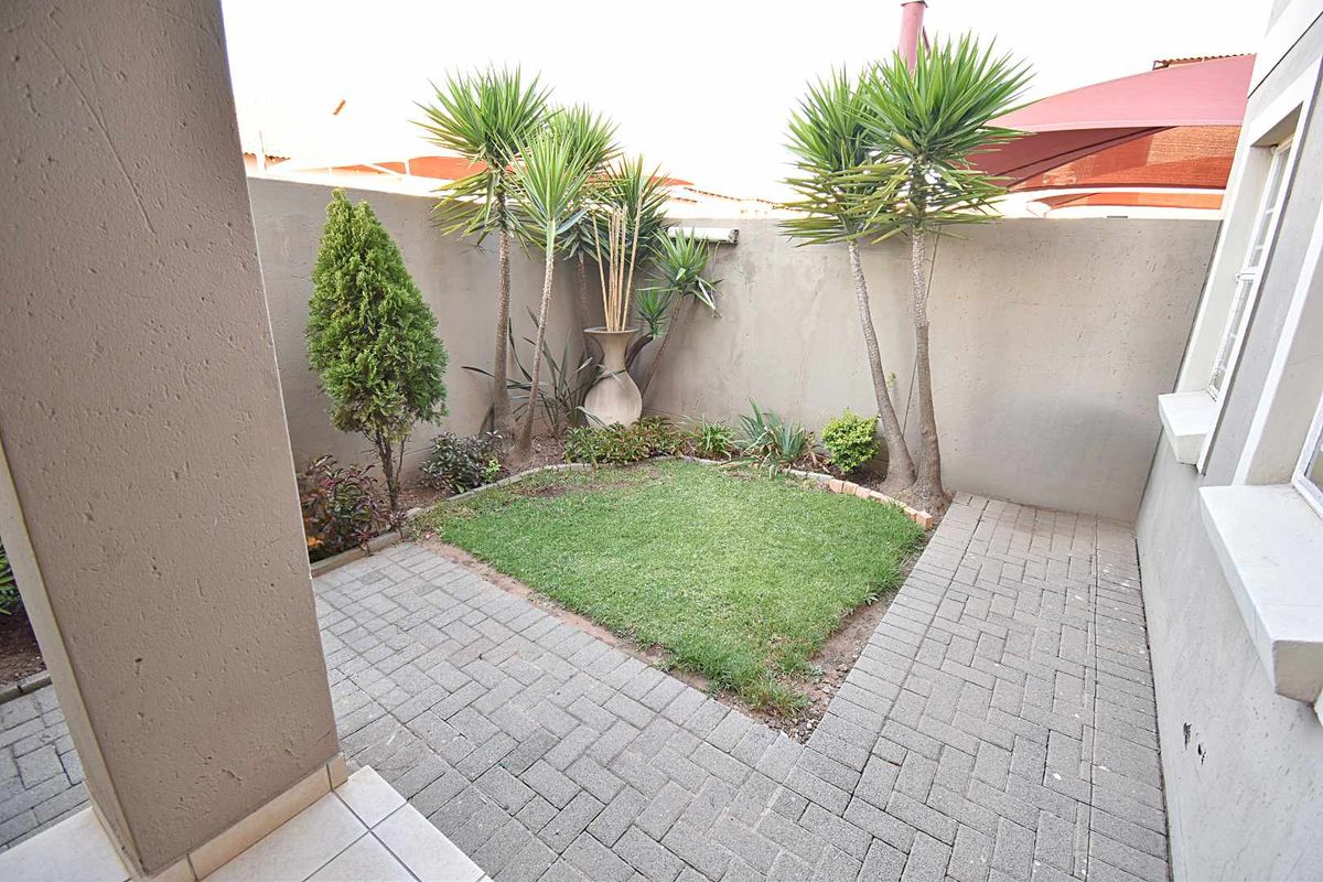 A private rear courtyard featuring a paved patio area, a small manicured lawn, and high boundary walls for added privacy.