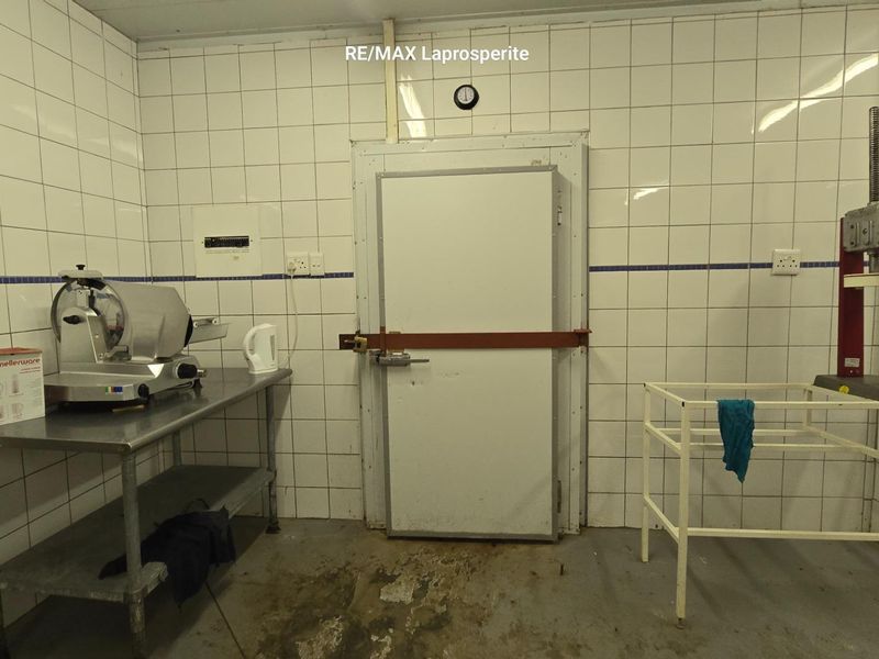 A functional utility or cold storage room featuring tiled walls, an industrial-style door, and concrete flooring, suitable for farm processing or storage needs.