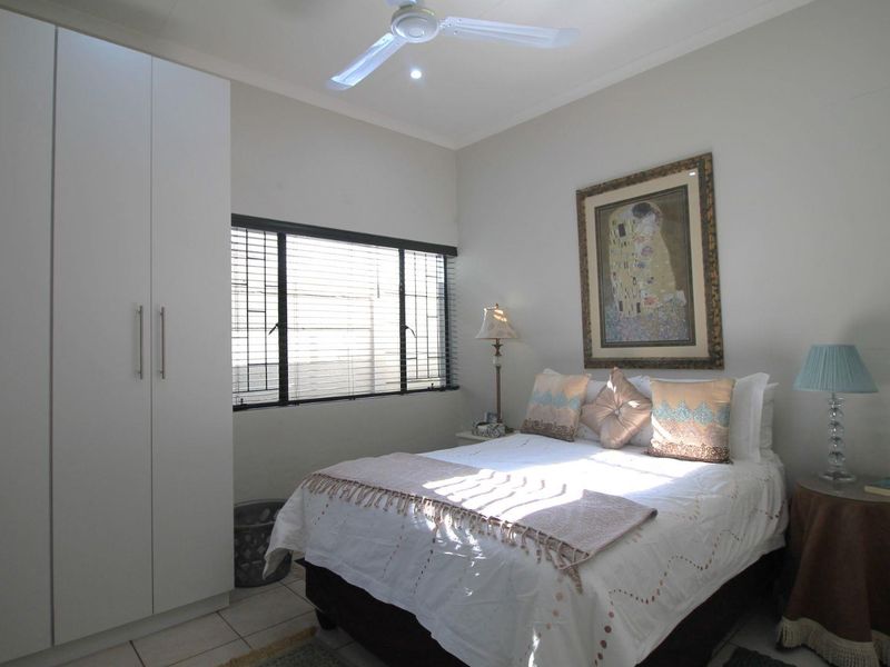 A well-maintained bedroom featuring a built-in wardrobe, ceiling fan, and tiled flooring, offering a clean and functional living space.
