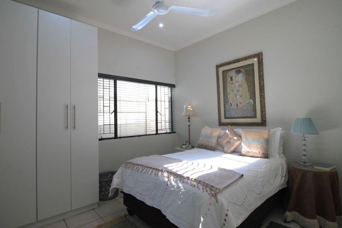 A well-maintained bedroom featuring a built-in wardrobe, ceiling fan, and tiled flooring, offering a clean and functional living space.