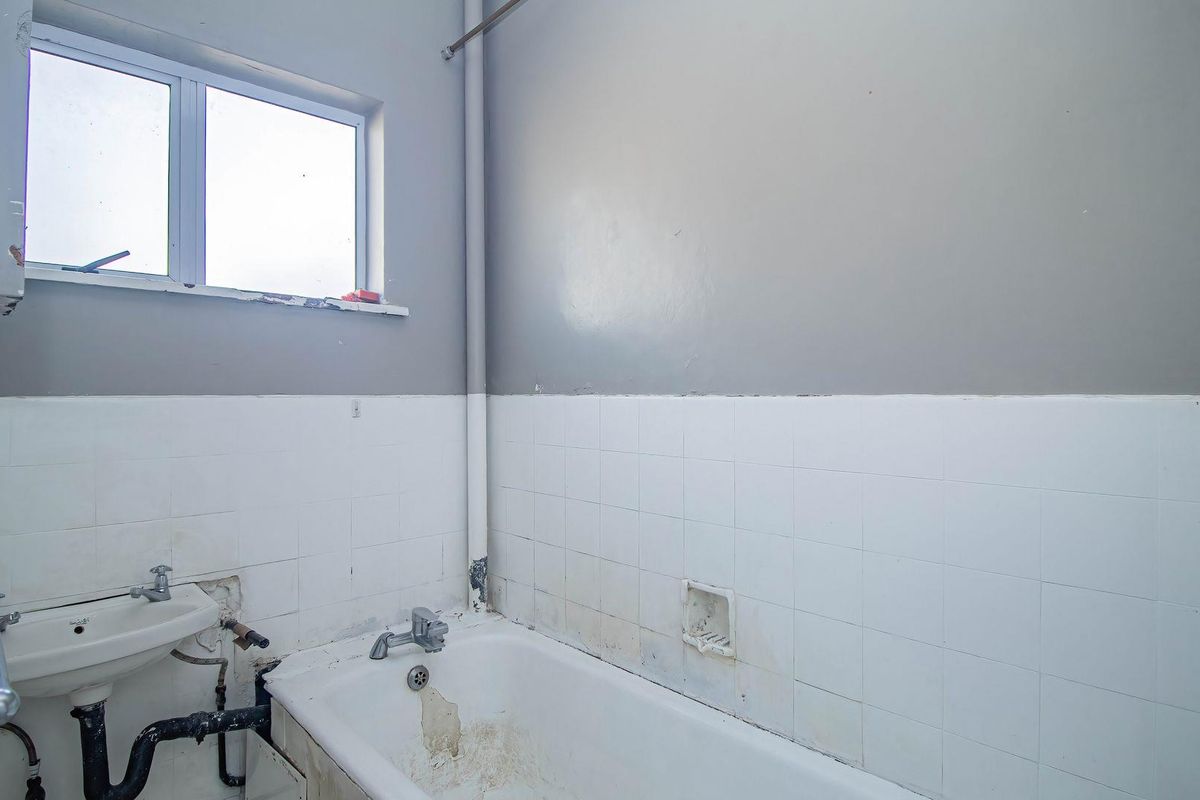 A dated bathroom featuring a bathtub, wall-mounted basin, and tiled splashbacks, requiring significant renovation and repair to restore functionality and aesthetic appeal.