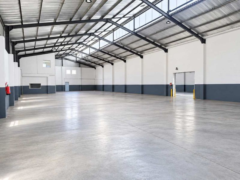 Spacious industrial warehouse featuring polished concrete floors, high exposed steel roof trusses, ample natural light from skylights, and integrated fire safety equipment.