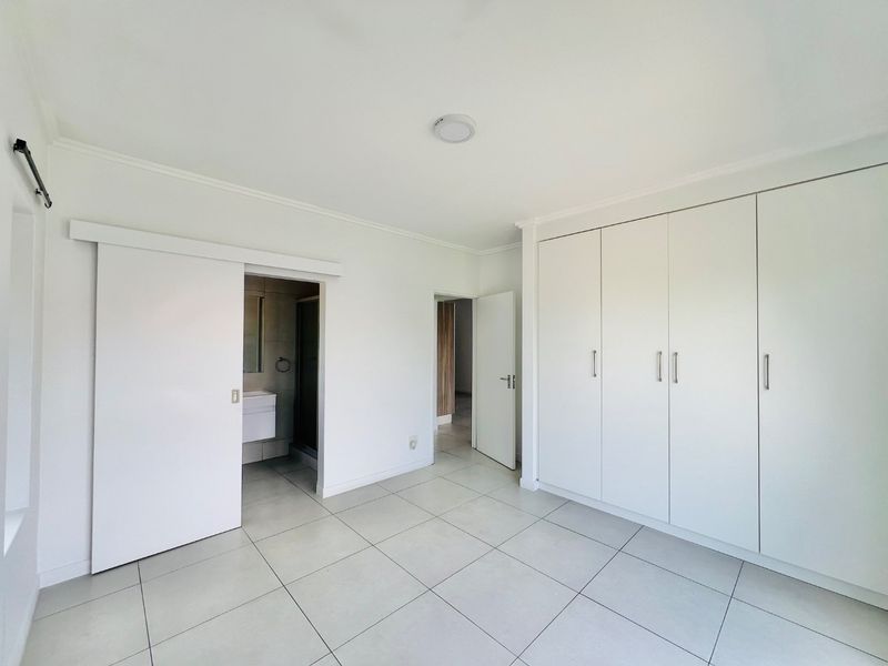 A bright, empty bedroom featuring neutral tiled flooring, ample built-in cupboard space, and direct access to an en-suite bathroom.