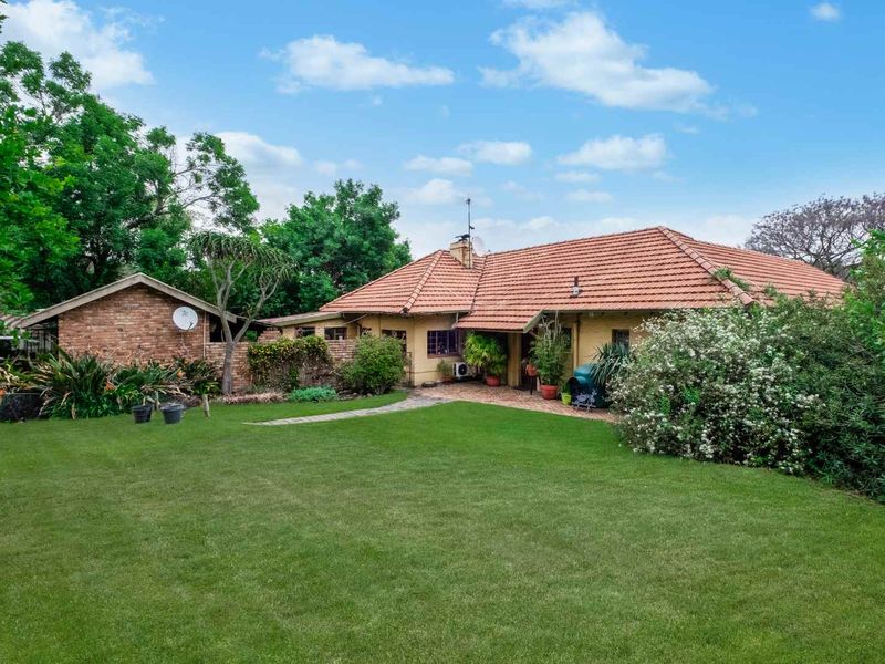 Rear view of the farm property featuring a spacious lawn, paved patio area, and traditional brick construction with a terracotta tiled roof.