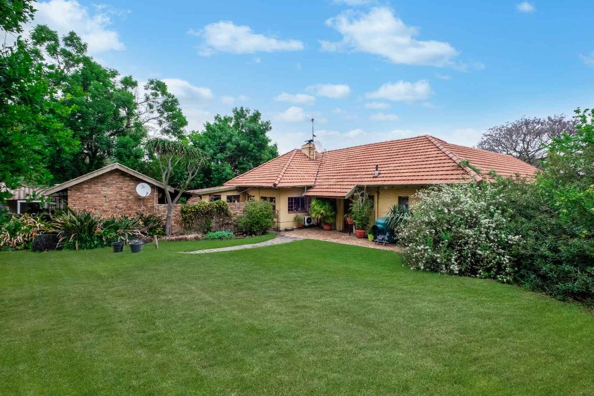Rear view of the farm property featuring a spacious lawn, paved patio area, and traditional brick construction with a terracotta tiled roof.