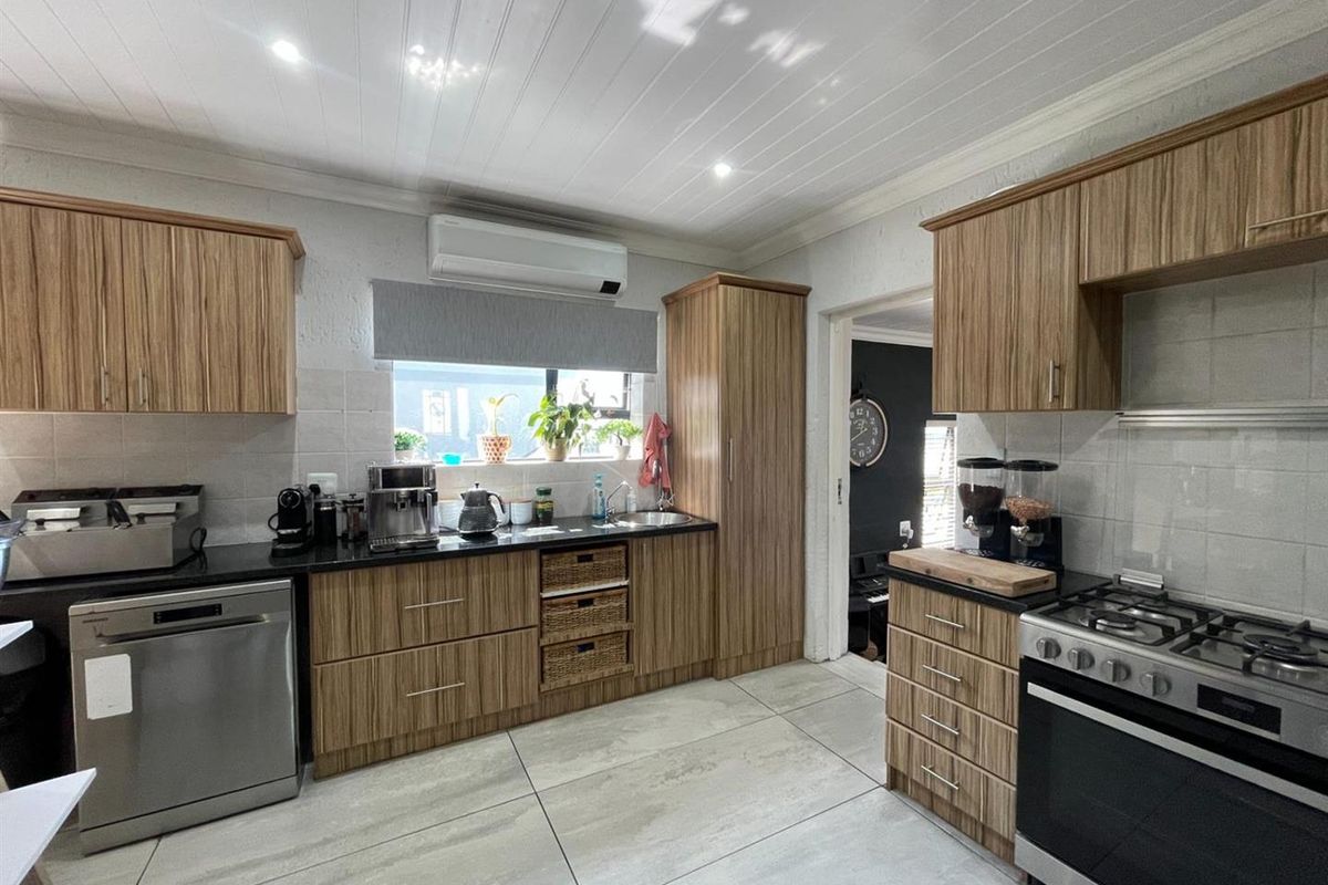 A well-maintained kitchen featuring wood-grain cabinetry, granite countertops, a gas stove, and large format floor tiles.
