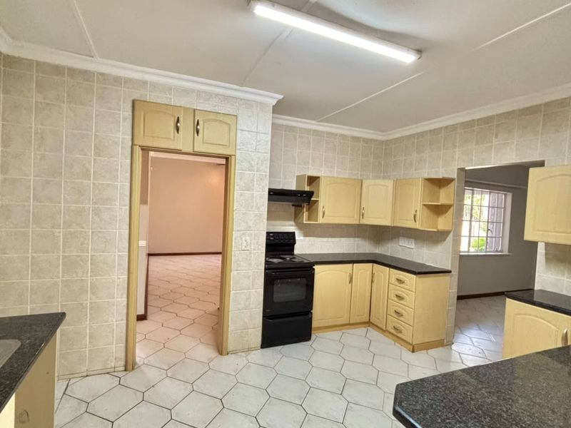 A functional kitchen featuring built-in cabinetry, laminate countertops, a freestanding stove with extractor fan, and tiled flooring throughout.