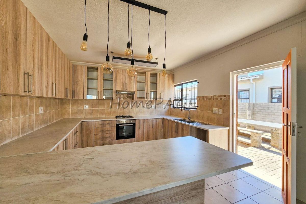 Modern kitchen featuring wood-look cabinetry, laminate countertops, built-in oven, gas hob, and direct access to an outdoor patio area.