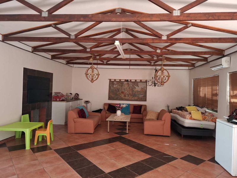 Spacious living area featuring exposed timber roof trusses, tiled flooring, a built-in fireplace, and a wall-mounted air conditioning unit.