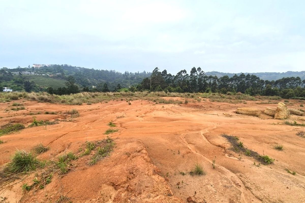 A wide-angle view of an undeveloped residential plot featuring natural terrain and distant hillside views.