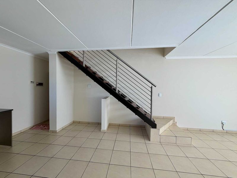 An open-plan living area featuring a modern staircase with a stainless steel balustrade and neutral tiled flooring throughout.