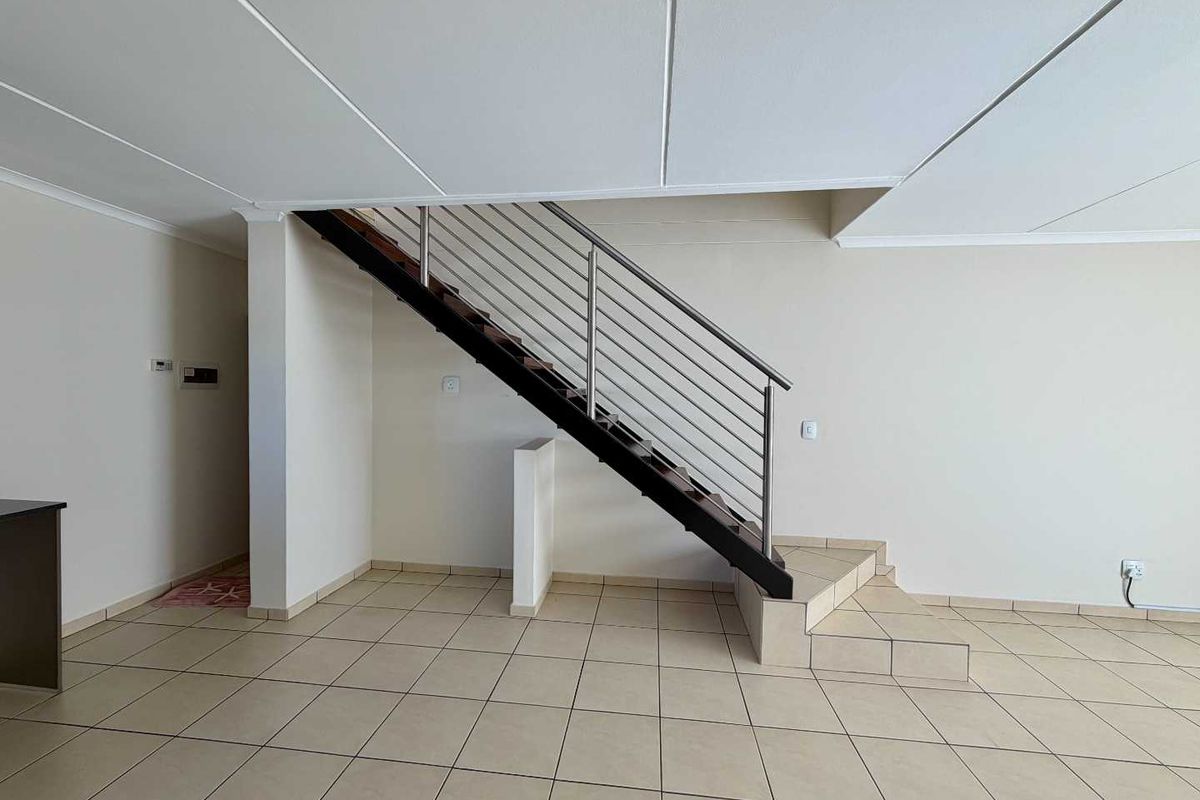 An open-plan living area featuring a modern staircase with a stainless steel balustrade and neutral tiled flooring throughout.