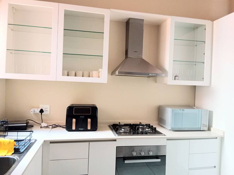 Modern kitchen featuring white cabinetry, glass-fronted display cupboards, stainless steel extractor fan, gas hob, and built-in oven with stone countertops.