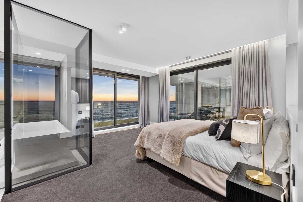 Modern bedroom featuring a glass-enclosed ensuite with a freestanding bathtub, floor-to-ceiling sliding doors, and expansive ocean views.