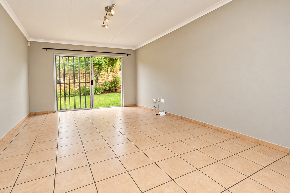 A bright, empty living room featuring neutral walls, ceramic floor tiles, and a sliding glass door providing direct access to the garden.
