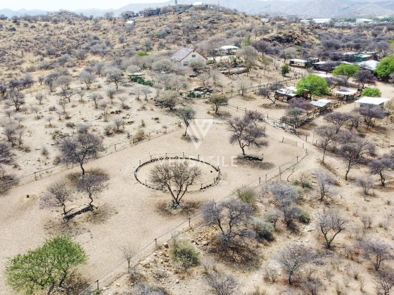 Aerial view of a small holding property featuring multiple outbuildings, fenced enclosures, and expansive natural landscape.