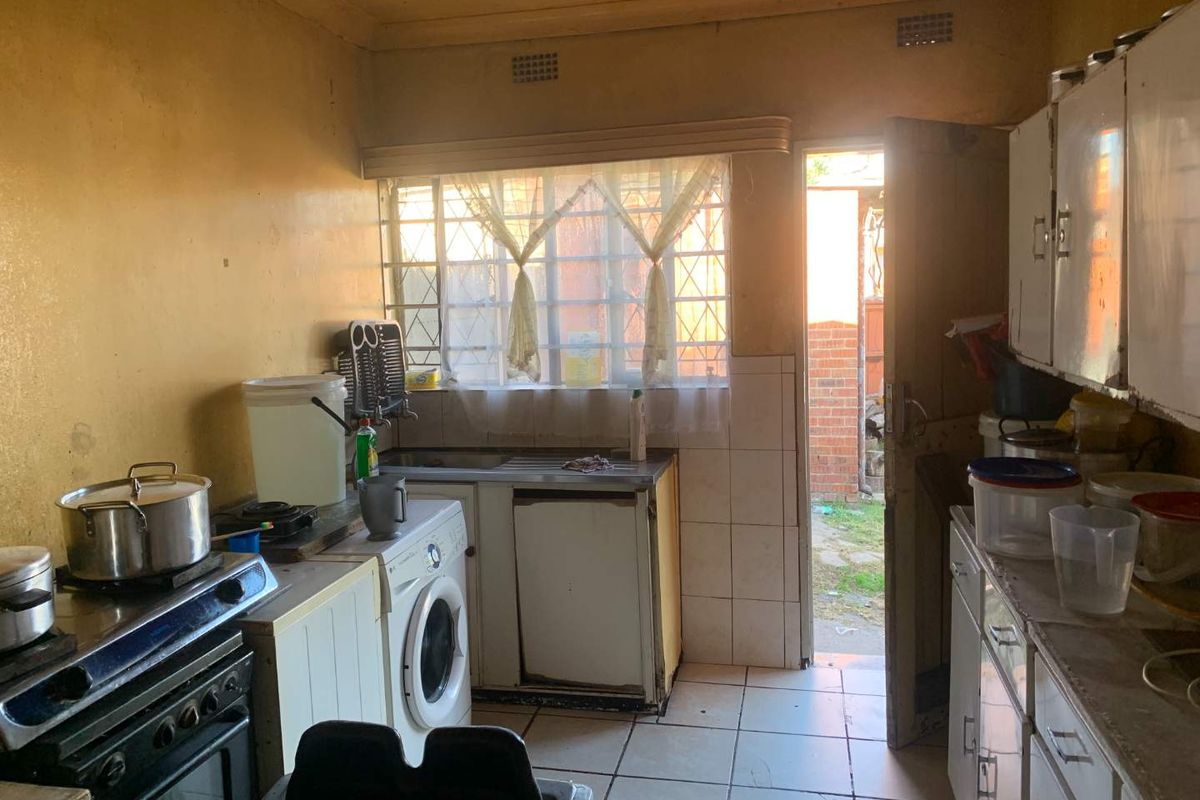 A dated kitchen featuring basic cabinetry, a stainless steel sink, and tiled flooring, with direct access to the rear exterior.