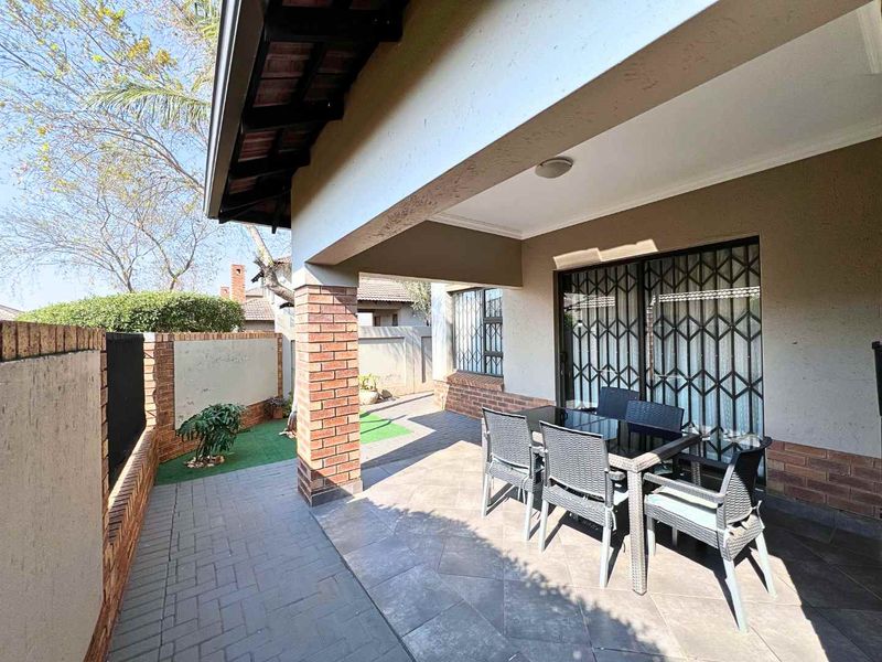 A covered patio area featuring tiled flooring, a brick support pillar, and a secure sliding door entrance to the interior.