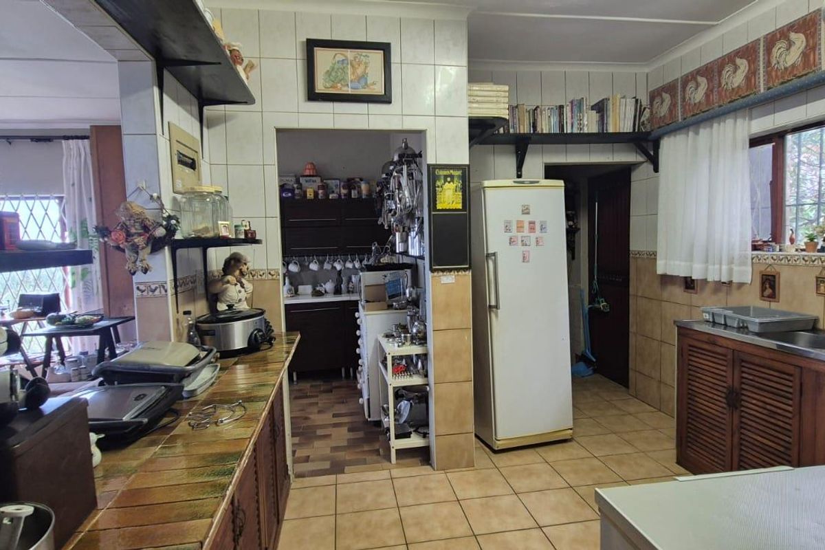 A functional kitchen featuring tiled flooring, a double basin sink, and ample built-in cabinetry, with an adjacent scullery area visible.