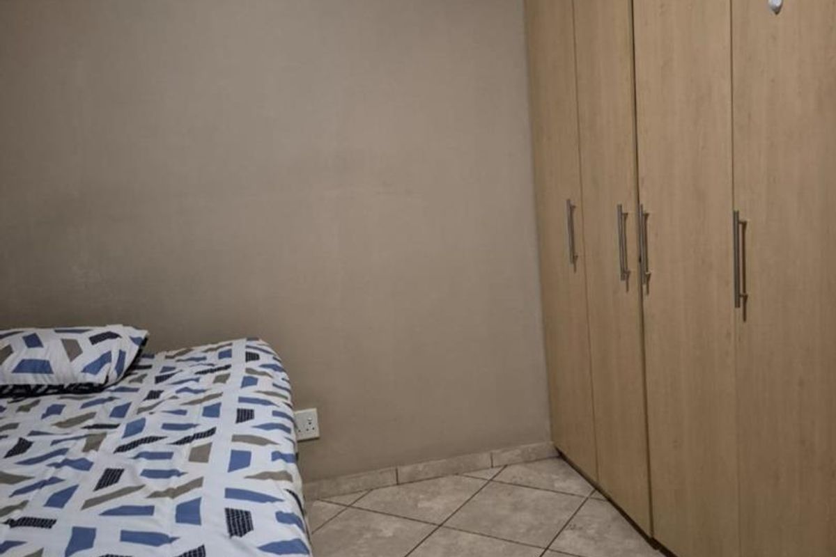 A bedroom featuring built-in light wood-finish wardrobes and tiled flooring.