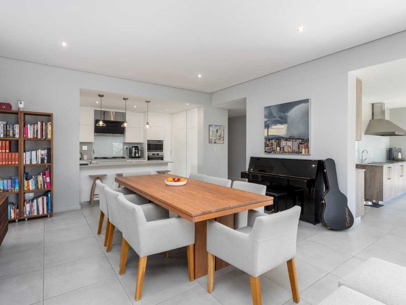 Modern open-plan dining area featuring sleek tiled floors, recessed lighting, and a seamless transition to a contemporary kitchen and scullery.