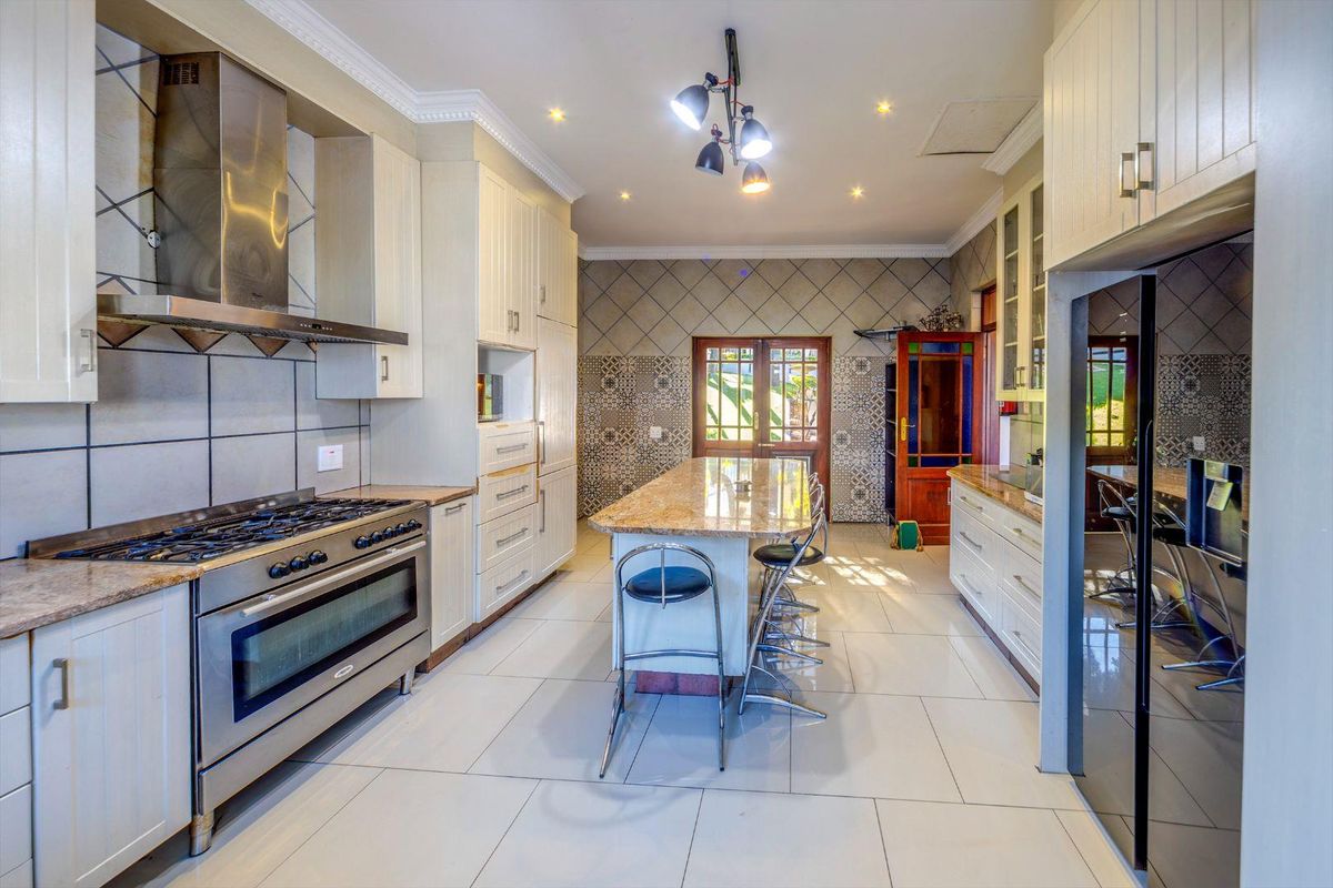 Spacious kitchen featuring a large central island with granite countertops, stainless steel gas range, extractor fan, and tiled flooring throughout.