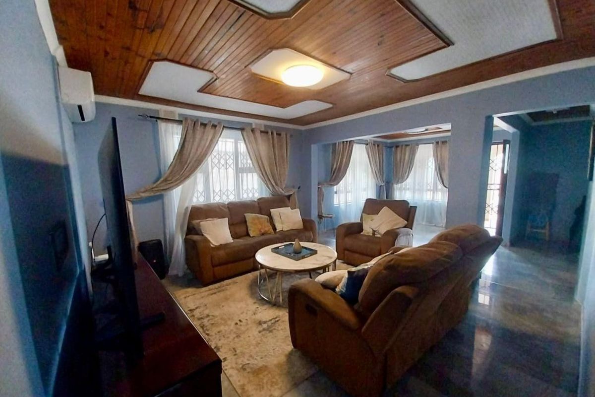 Spacious living room featuring a distinctive timber panelled ceiling, tiled flooring, and large windows fitted with security bars, offering a comfortable and functional layout.
