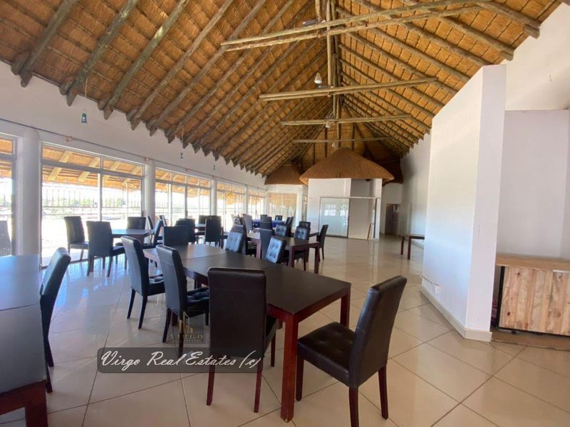 Spacious dining area featuring a high vaulted thatched roof with exposed timber trusses, tiled flooring, and large glass sliding doors providing ample natural light.