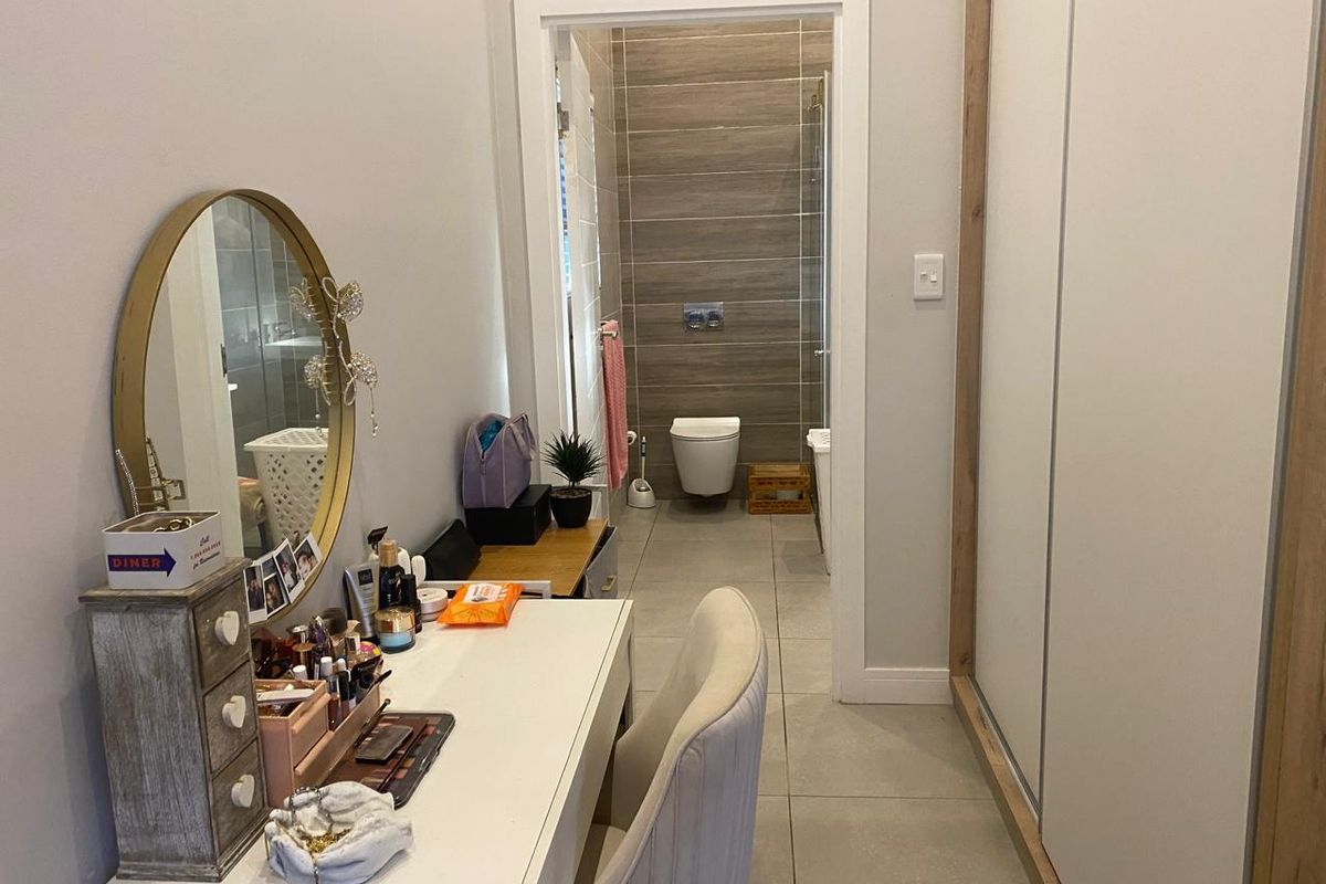 A modern bedroom featuring built-in wardrobes, tiled flooring, and direct access to a contemporary en-suite bathroom with a wall-mounted toilet and shower.