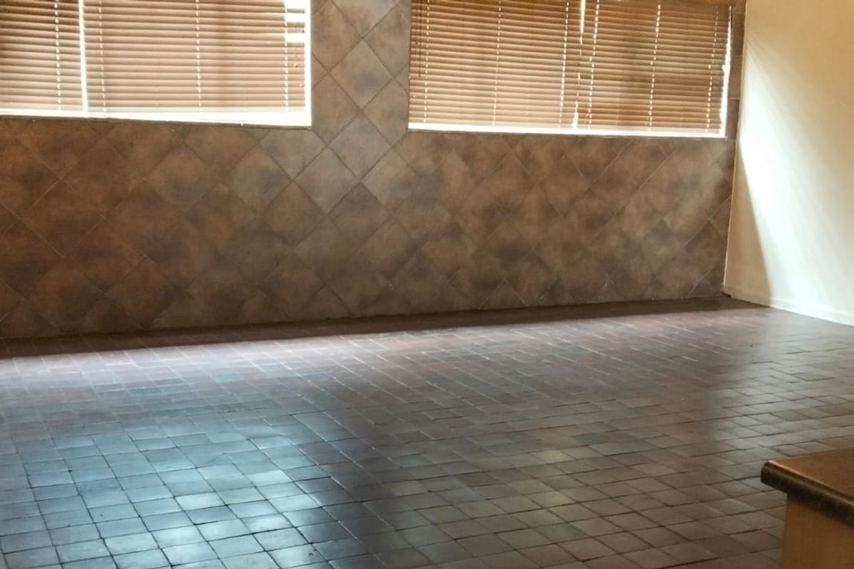 A spacious kitchen area featuring dark tiled flooring and decorative wall tiling, offering a functional layout ready for modernization.