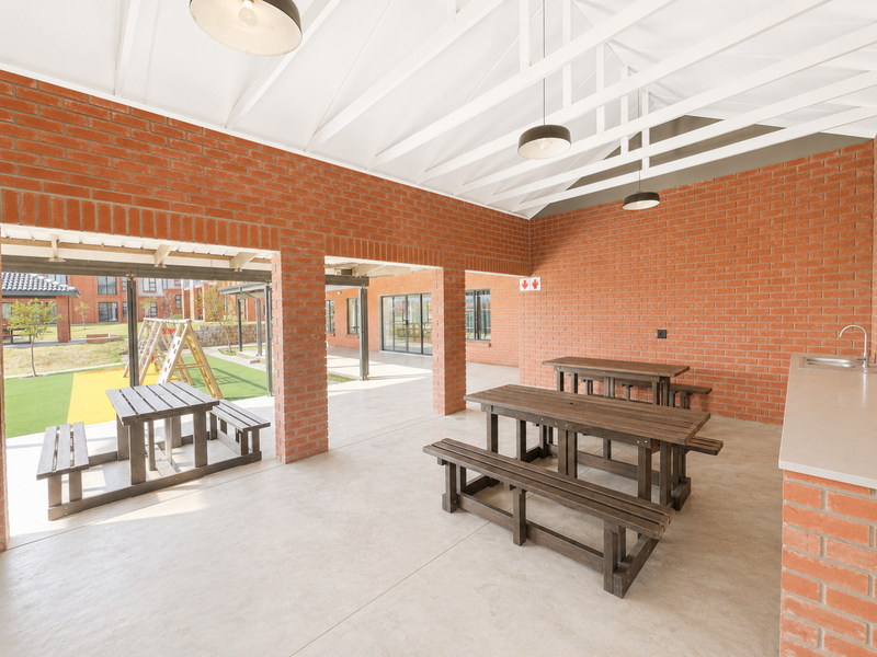 A spacious covered outdoor patio featuring exposed brickwork, timber roof trusses, concrete flooring, and a built-in sink area, ideal for communal gatherings.