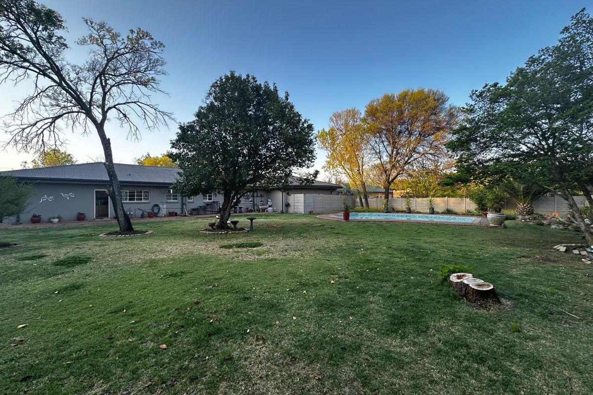 Spacious rear garden featuring a swimming pool, established trees, and a view of the rear building elevation with a paved patio area.