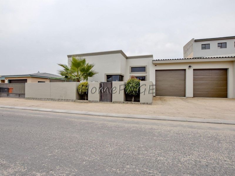 Modern single-story residential property featuring a double garage, secure boundary wall with pedestrian gate, and a paved driveway.