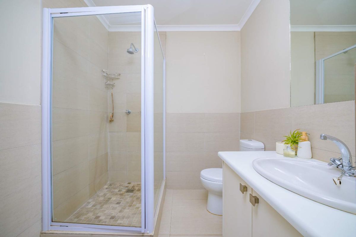 A clean and functional bathroom featuring a glass-enclosed shower, a vanity with a basin, and a toilet, finished with neutral wall and floor tiles.