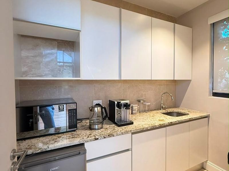 A compact, well-maintained scullery featuring granite countertops, white cabinetry, a stainless steel sink, and neutral tiled finishes.