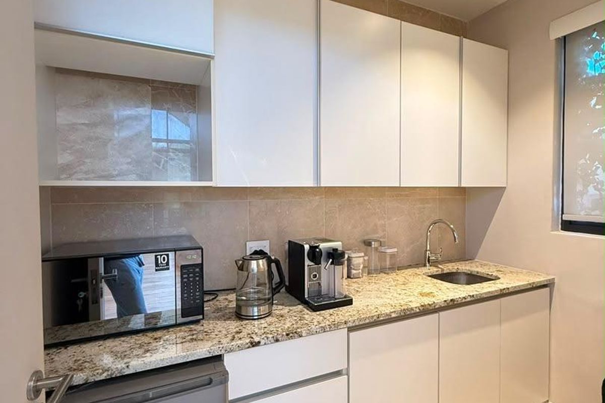 A compact, well-maintained scullery featuring granite countertops, white cabinetry, a stainless steel sink, and neutral tiled finishes.