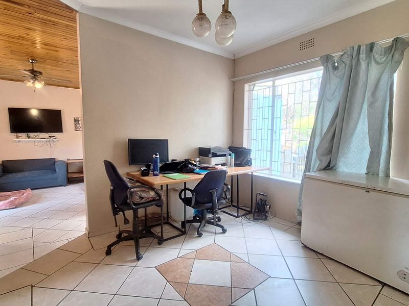 Open plan living area featuring tiled flooring, security bars on windows, and a view into the adjacent living space with wood-paneled ceiling.