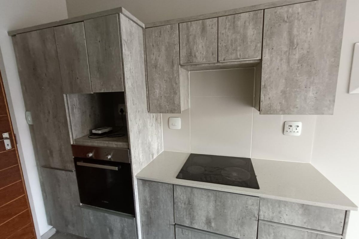 Modern kitchen featuring concrete-look cabinetry, stone-style countertops, a built-in oven, and a sleek electric hob with a tiled splashback.