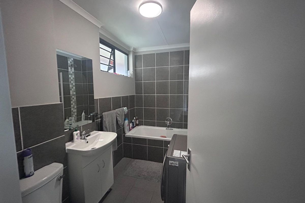 A functional bathroom featuring a built-in bathtub, vanity cabinet with basin, toilet, and modern grey wall tiling.