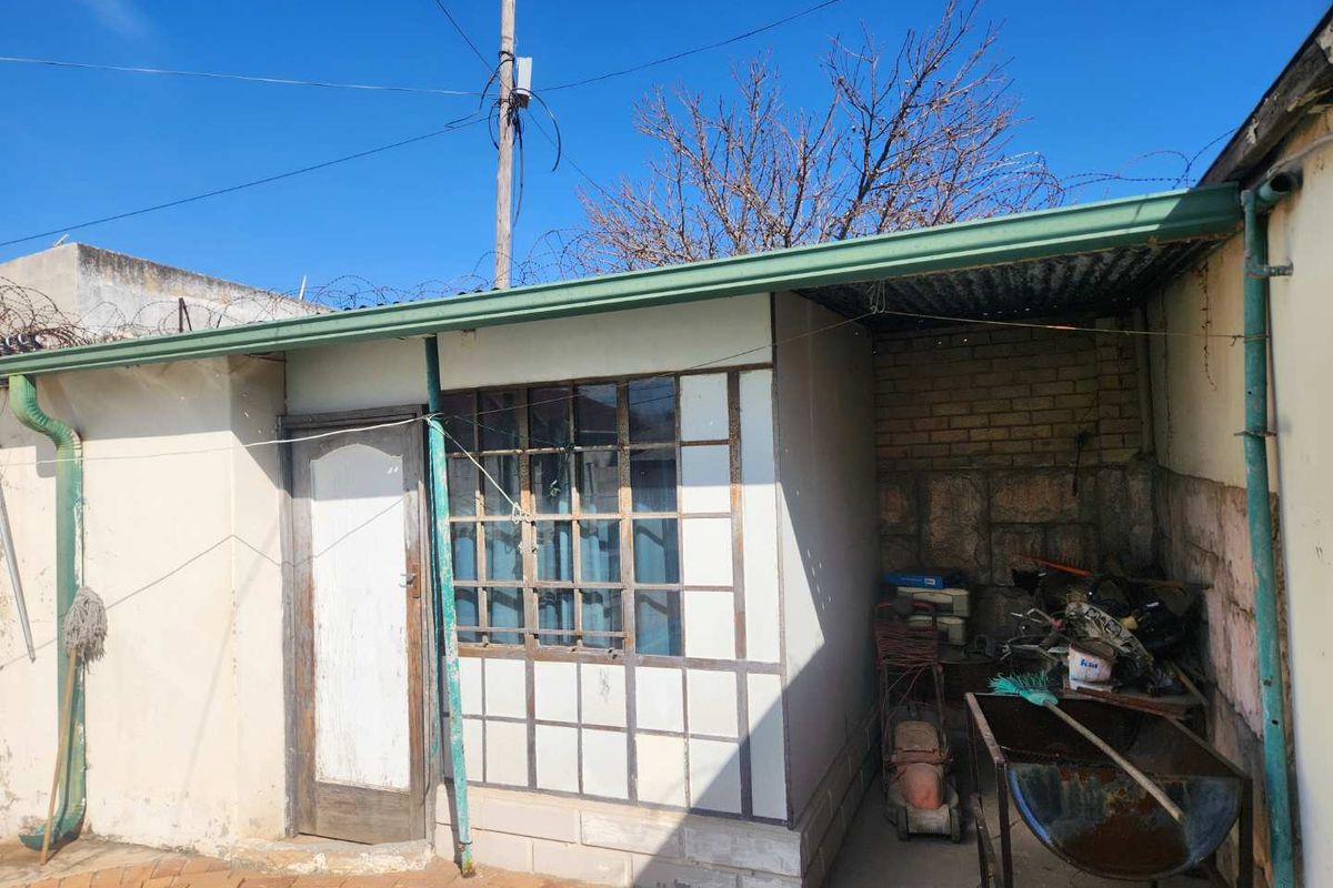 Rear exterior view of the property featuring a covered patio area, brick walling, and a multi-pane window with a timber door.