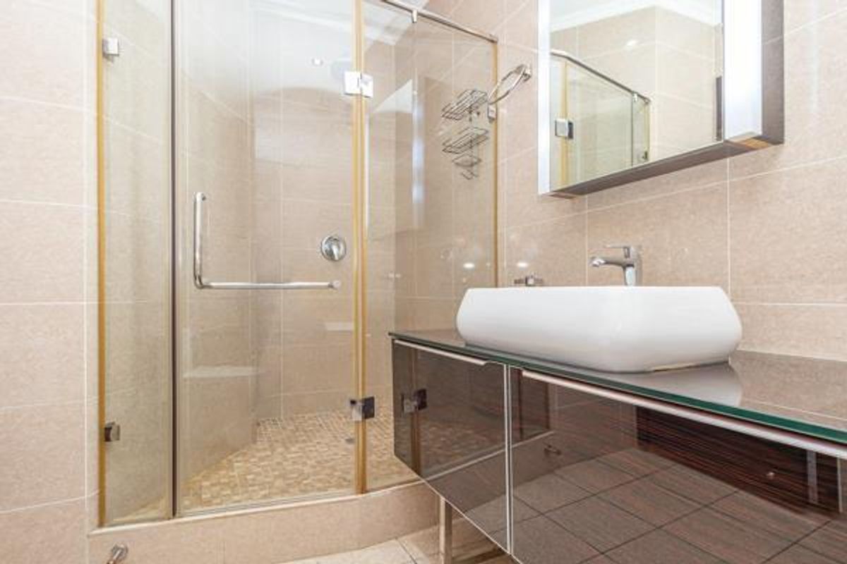 Modern bathroom featuring a glass-enclosed shower, a contemporary vessel sink mounted on a sleek vanity, and neutral wall tiling.