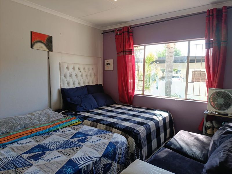 A bedroom featuring a large window with security burglar bars and decorative coving, providing natural light and a view of the exterior.