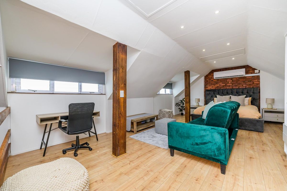 Spacious attic-style bedroom featuring exposed brick feature wall, timber support beams, recessed lighting, and a wall-mounted air conditioning unit.