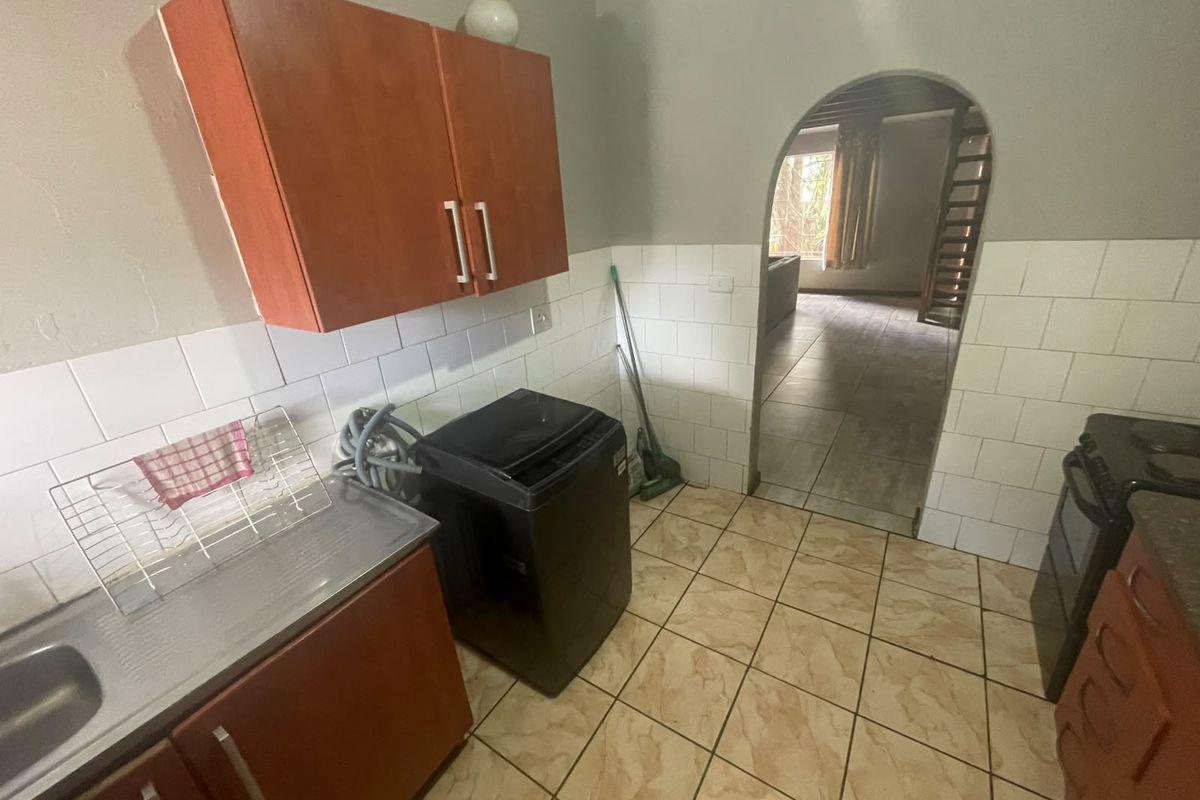 A functional kitchen area featuring built-in cabinetry, a stainless steel sink, and tiled finishes, leading through an arched doorway to the adjacent living space.