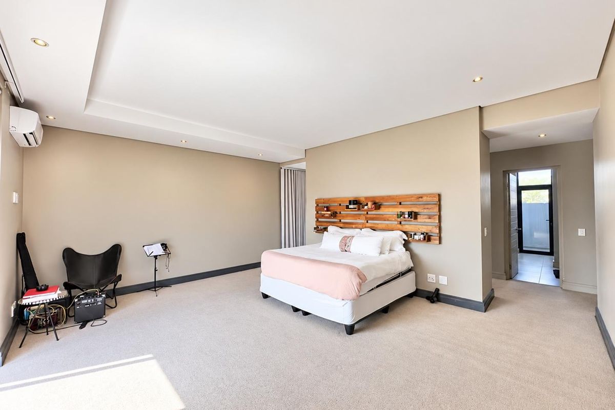 Spacious bedroom featuring neutral wall tones, recessed ceiling with downlights, carpeted flooring, and a wall-mounted air conditioning unit.