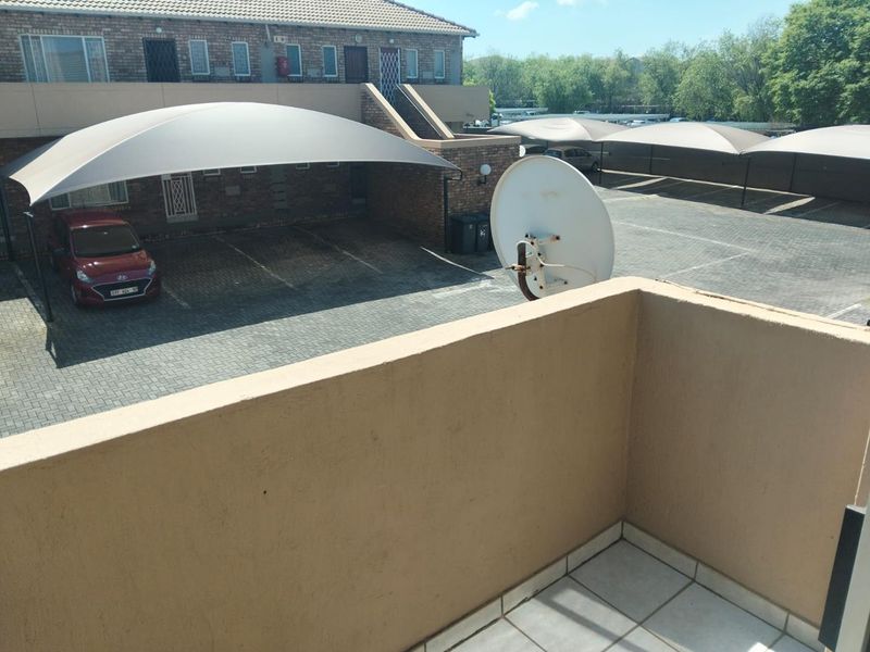 A balcony overlooking the apartment complex parking area, featuring tiled flooring and a parapet wall.