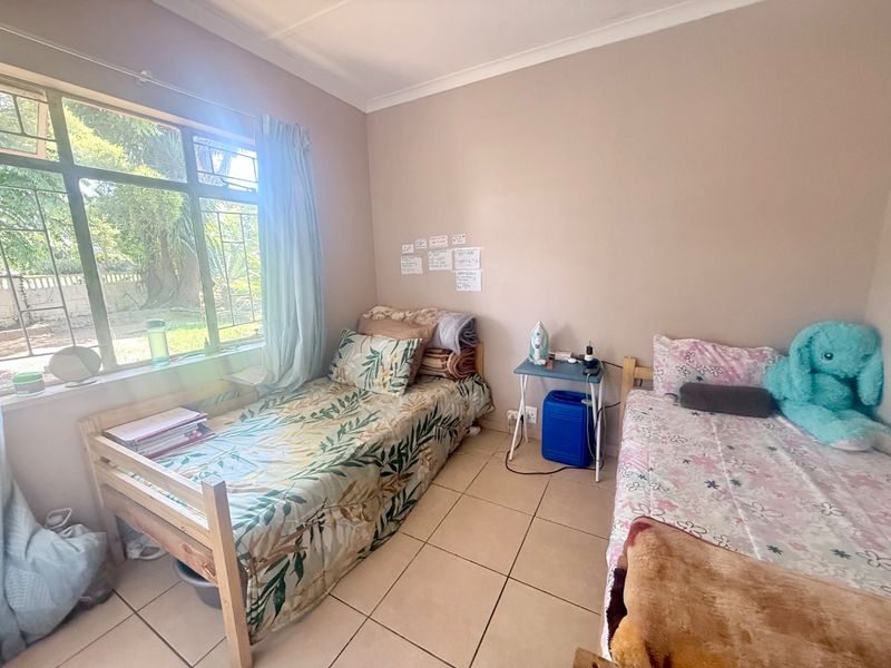 A functional bedroom featuring tiled flooring and a large window that provides natural light and garden views.