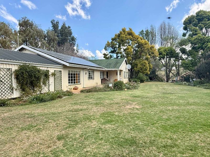 Rear view of the farm property featuring a spacious lawn, established garden, and a combination of metal and tiled roofing with solar panels.