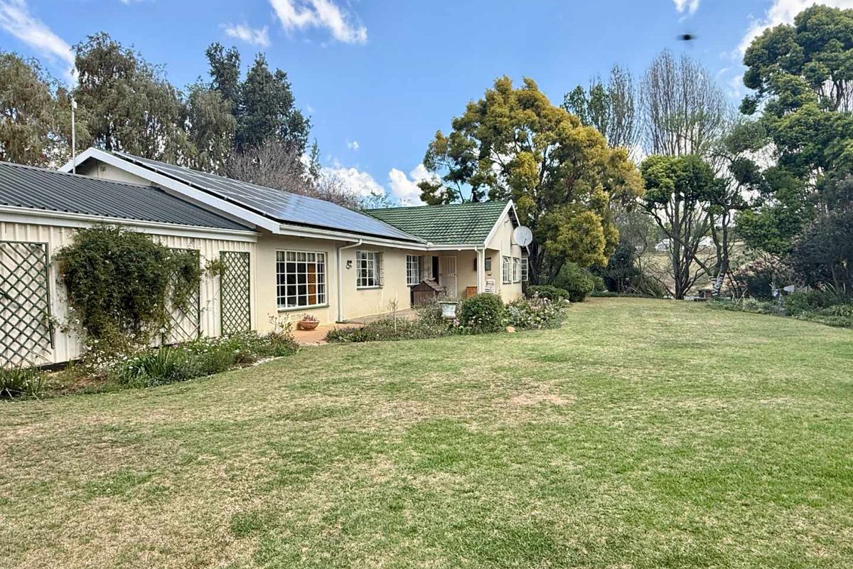 Rear view of the farm property featuring a spacious lawn, established garden, and a combination of metal and tiled roofing with solar panels.