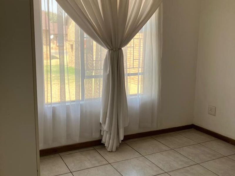 A bright, empty bedroom featuring neutral tiled flooring and a large window with natural light, providing a clean canvas for personalization.